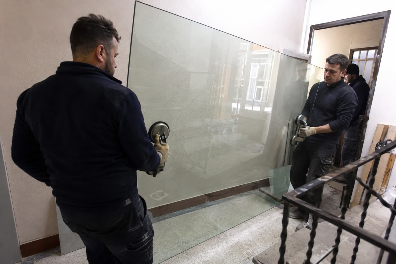 Монтажники заносят большое стеклянное полотно по коридору
